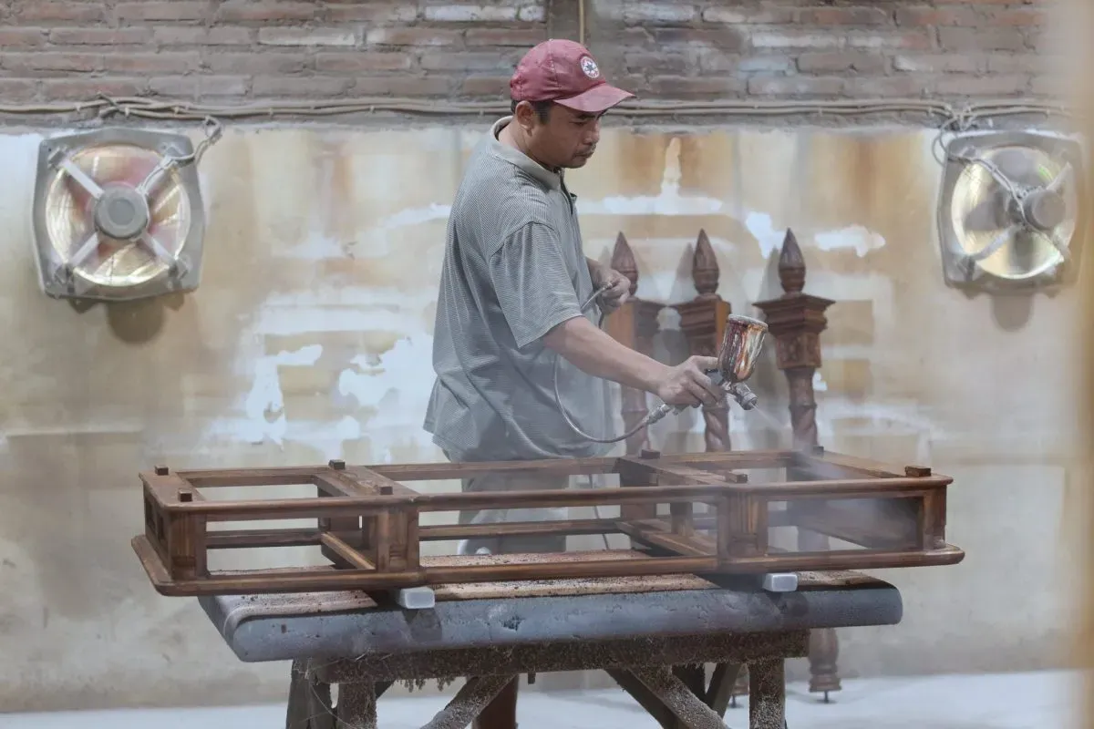 Worker spray painting wooden furniture in workshop