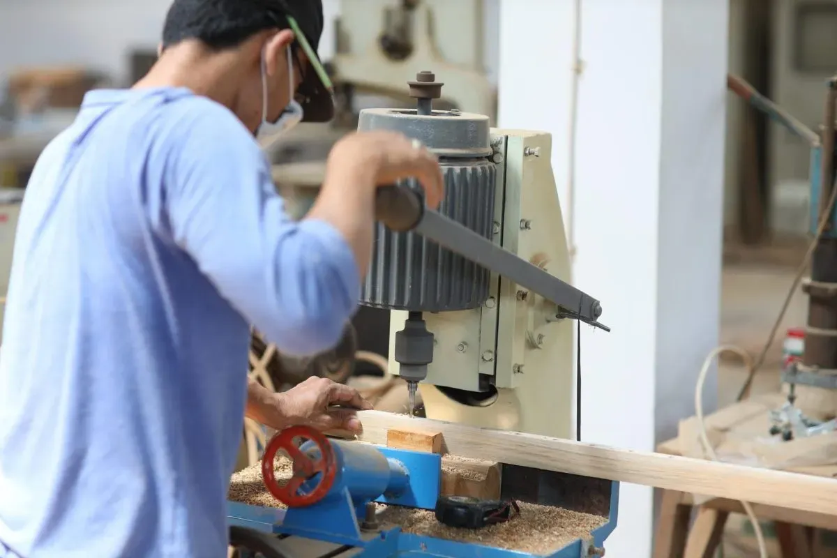 Worker using drill press in woodworking shop