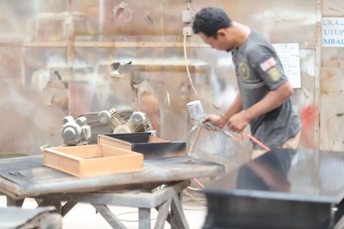 Worker spray painting wooden furniture pieces