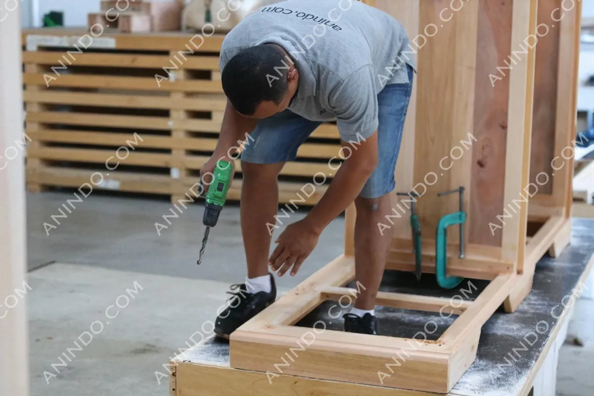 Carpenter drilling wood frame in workshop